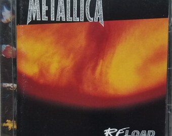 May include: A Metallica ReLoad music CD case featuring a square cover with a central abstract design of swirling orange, red, and yellow colors against a black background. The word METALLICA is printed in white at the top, and RE-LOAD is at the bottom.