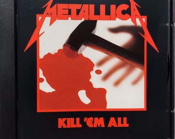 May include: A black and red CD case with the band name "Metallica" in white text and the album title "Kill 'Em All" in red text. The album cover features a bloody hand with a hammer on top of it.