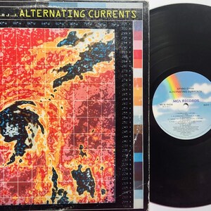 May include: A vinyl record album by Spyro Gyra, titled "Alternating Currents." The album cover features a colorful, abstract design with red, orange, and blue hues. The record itself is black, with a label showing a rainbow and the MCA Records logo.