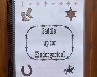 May include: A spiral-bound notebook with a white cover featuring cowboy-themed illustrations. The cover includes images of cowboy boots, a sheriff's star, a horseshoe, and a cowboy riding a horse. Text reads "Saddle up for Kindergarten!"