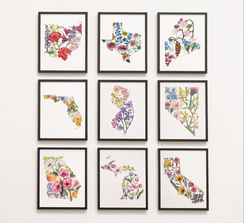 May include: A set of nine framed prints featuring floral designs in the shape of different US states. The prints are all in black frames and have white backgrounds. The flowers are painted in watercolor and are in shades of pink, purple, yellow, and blue.