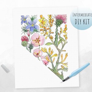 May include: A watercolor painting of a heart-shaped arrangement of flowers, including blue, pink, yellow, and green flowers. The text "INTERMEDIATE DIY KIT" is in a blue circle in the upper right corner of the image.