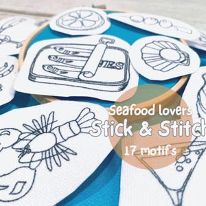 May include: A collection of white fabric patches with black embroidered seafood designs, including a lobster, sardines, and a cocktail. The patches are arranged around an embroidery hoop. Text reads "Seafood lovers Stick & Stitch 17 motifs."