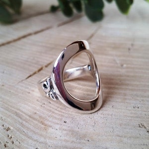 May include: A silver ring with a large oval opening. The ring has a decorative design on the side.