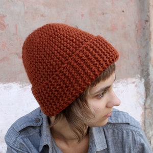 Può includere: Una persona che indossa un berretto di lana color ruggine e una camicia grigia abbottonata.