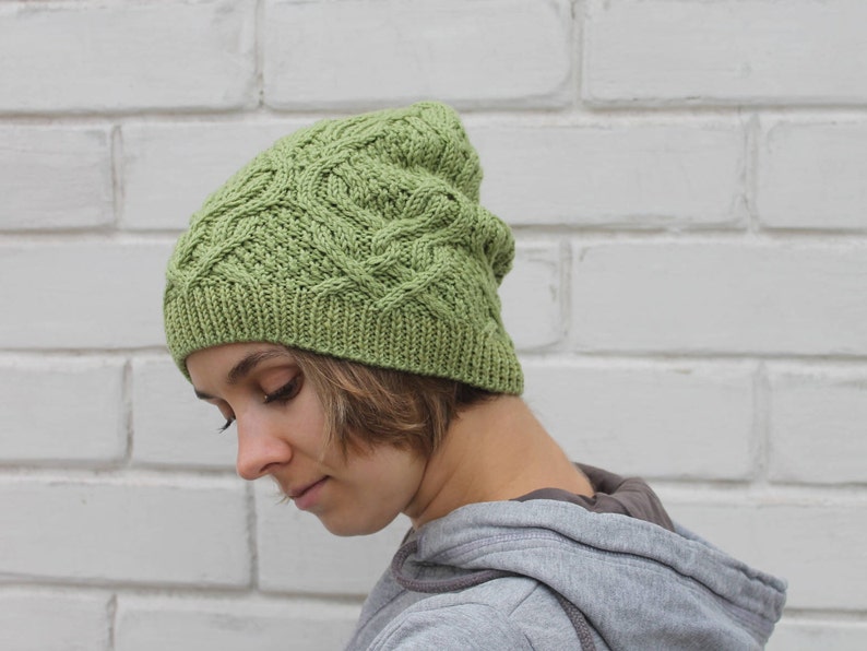 May include: A green knitted hat with a cable knit pattern. The hat is worn by a person with brown hair.
