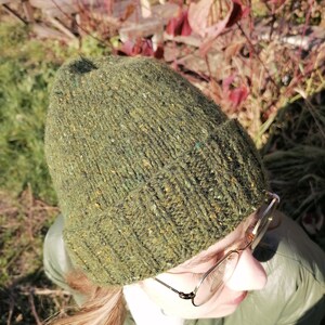 May include: A green knit beanie with flecks of color throughout. The hat is made of a textured yarn and has a folded ribbed brim. The beanie is shown from a high angle, with the top of the head and part of the face visible.