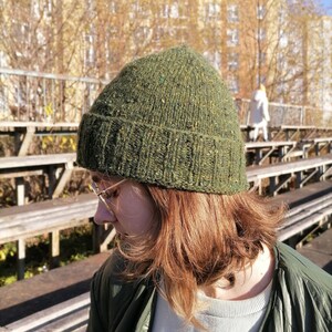 May include: A green knit beanie with flecks of color. The hat is made of a textured yarn and has a ribbed folded brim. The beanie is a warm accessory for cold weather.