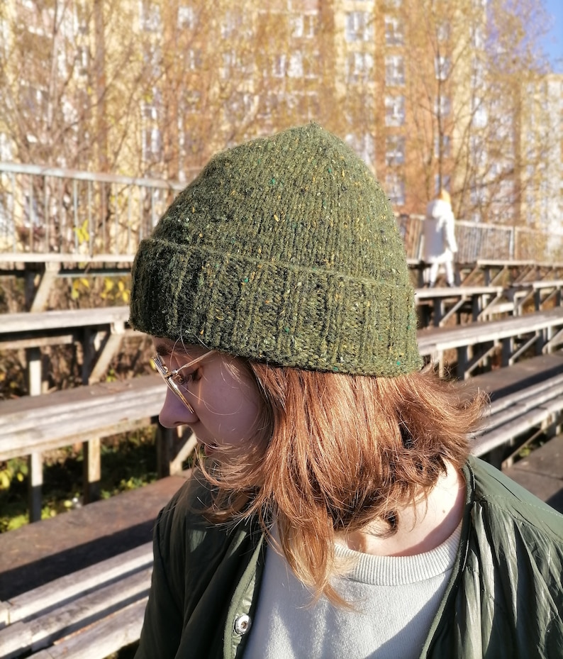 May include: A green knit beanie with flecks of color. The hat is made of a textured yarn and has a ribbed folded brim. The beanie is a warm accessory for cold weather.