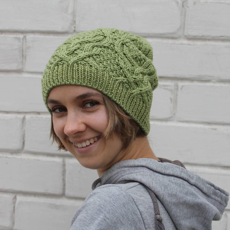 May include: A green knitted hat with a cable knit pattern. The hat is worn by a person with short brown hair.