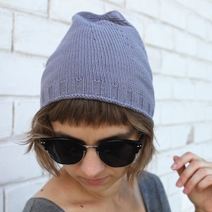 Pode incluir: Uma pessoa usando um gorro de tricô cinza e óculos de sol pretos. O gorro tem uma textura canelada e uma aba dobrada.