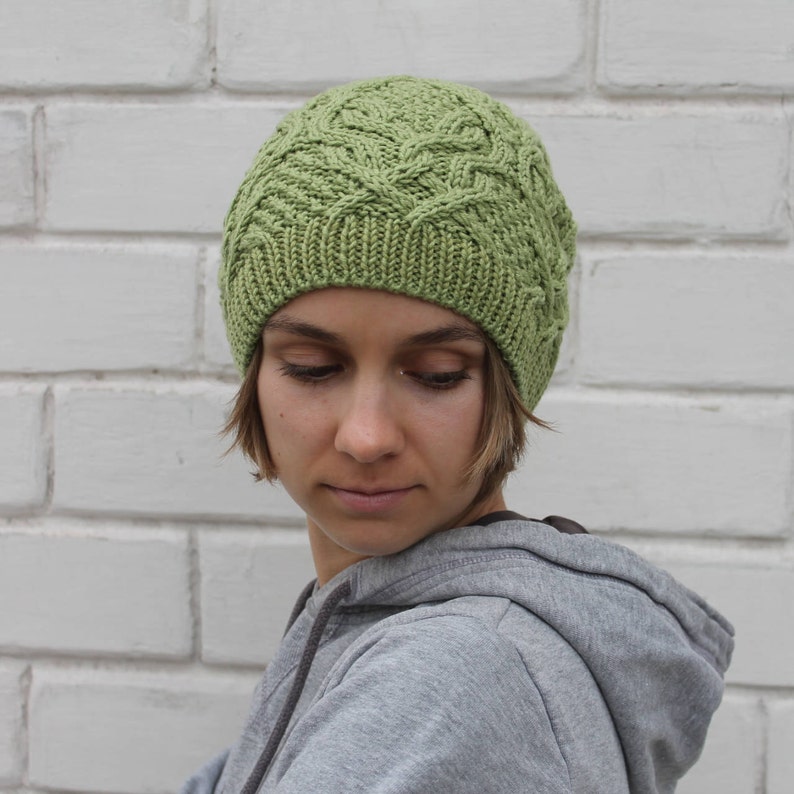 May include: A green knitted hat with a cable knit pattern. The hat is worn by a person with short brown hair.