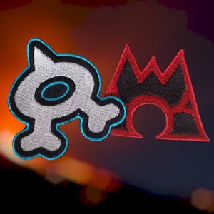 May include: Two embroidered patches, one white with a blue outline in the shape of a stylised skull and the other red with a black outline in the shape of a mountain.