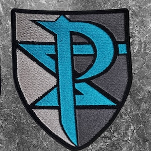 Könnte beinhalten: Ein gestickter Aufnäher in Form eines Schildes mit einem stilisierten Buchstaben "P" in Blau auf grauem und weißem Hintergrund.