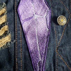 以下が含まれることがあります： デニムジャケットにクリスタル型の紫色の刺繍パッチ