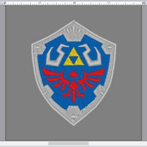 May include: A blue and red embroidered patch featuring the iconic Triforce symbol from the Legend of Zelda video game series. The shield is surrounded by a silver border and has a stylized bird design.