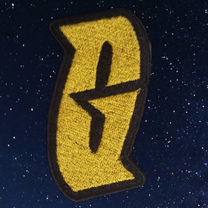 Puede incluir: Un parche bordado amarillo con una estrella negra dentro de una forma curva.