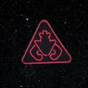 Puede incluir: Un parche bordado rojo en forma de triángulo con una silueta negra de un cangrejo en su interior. El parche está sobre un fondo negro con estrellas blancas.