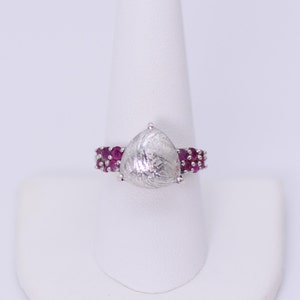 May include: A silver ring with a pear-shaped, textured gemstone surrounded by a band of small, pink gemstones.