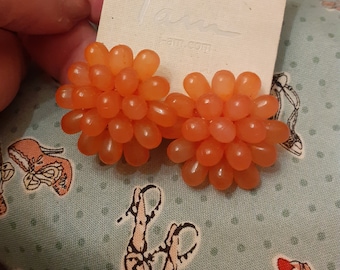 May include: A pair of orange cluster earrings. The earrings are made of small, round beads that are clustered together to form a flower shape. The earrings are on a white card with the word "love" printed on it.