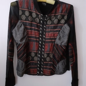 May include: A black and red patterned long-sleeved shirt with a zipper closure and silver grommets. The shirt has a mesh overlay and a gray fabric detail on the front.