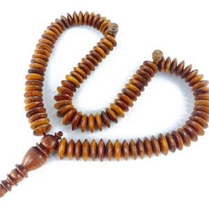 May include: A brown wooden prayer beads necklace with a tassel. The beads are shaped like small, flat ovals and are strung together on a thin cord. The tassel is made of a red cord and is attached to the end of the necklace.