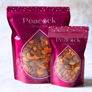 May include: Two bags of Peacock Snacks, one large and one small, are displayed. The bags are a deep magenta with a clear, teardrop-shaped window showing a mix of nuts. The text "Peacock Snacks" is printed in white.