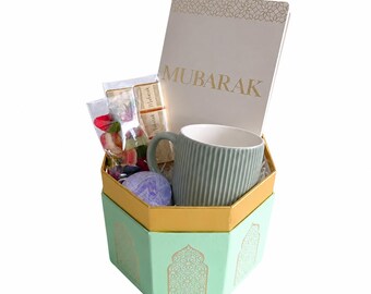 May include: A hexagonal gift box in mint green with gold accents containing a ribbed sage green mug, a white card with the gold text MUBARAK, a small gold-toned item, and a clear bag of colorful dried flower petals and a purple bath bomb.