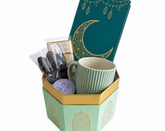 May include: A hexagonal gift box in light green with gold arch patterns contains a ribbed light green mug, a clear bag of dark brown dates, a small white rectangular box, and a dark green notebook featuring gold lanterns and a crescent moon.