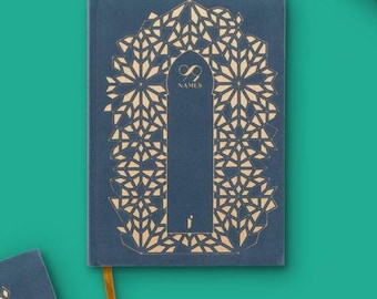 May include: A dark blue hardcover journal featuring a gold-colored geometric pattern surrounding a central archway design. The text 99 NAMES is printed in gold near the top of the arch, with a small gold letter i at the bottom of the cover.