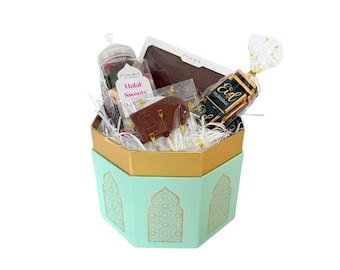 May include: A gift box with a mint green and gold exterior, filled with sweets. The box contains a jar of Halal Sweets, chocolate bars, and a wrapped candy with "Eid Mubarak" on it. The box has a decorative pattern.