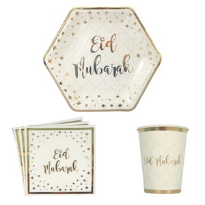 Op de afbeelding: Een set gouden en witte wegwerp-partybenodigdheden met de tekst "Eid Mubarak". De set bevat een zeshoekig papieren bord, een papieren beker en vier servetten.