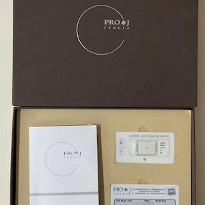 May include: A white diamond identification report card with the Pro J Italia logo. The report card includes the diamond's shape, weight, color grade, clarity grade, and cut grade. The diamond is a round brilliant cut, weighs 0.04 carats, has a color grade of G, a clarity grade of SI2, and a cut grade of Very Good.