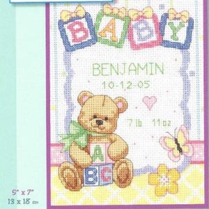 May include: Cross-stitch baby announcement with the name "BENJAMIN" and birthdate 10-12-05. A teddy bear holds ABC blocks. The announcement includes a butterfly, flower, and heart. The dimensions are 13 x 18 cm and the weight is 7 lb 11 oz.