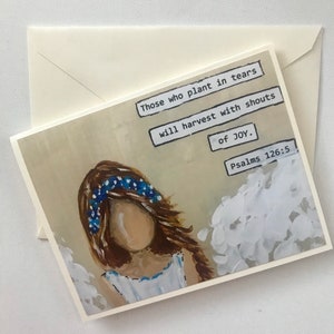 May include: A greeting card featuring a painting of a faceless figure with brown hair and a blue floral crown, wearing a white dress. The text reads: Those who plant in tears will harvest with shouts of JOY. Psalms 126:5. An envelope is included.