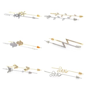 Könnte beinhalten: Sechs Paar Ohrringe mit verschiedenen Designs. Jedes Paar besteht aus einem kleinen, klaren Kristallstecker und einem längeren, baumelnden Teil mit verschiedenen Designs, darunter eine Hand, ein Blitz, Blätter und das Wort "Love".