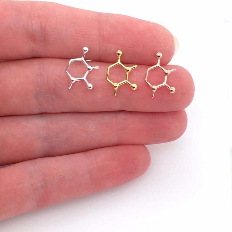 May include: Three small, hexagonal-shaped charms with round beads at each corner. The charms are silver, gold, and rose gold.
