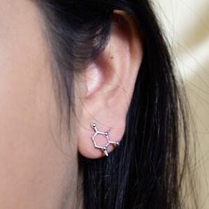 May include: A silver earring shaped like a chemical molecule. The earring is worn in the left ear of a person with long black hair.