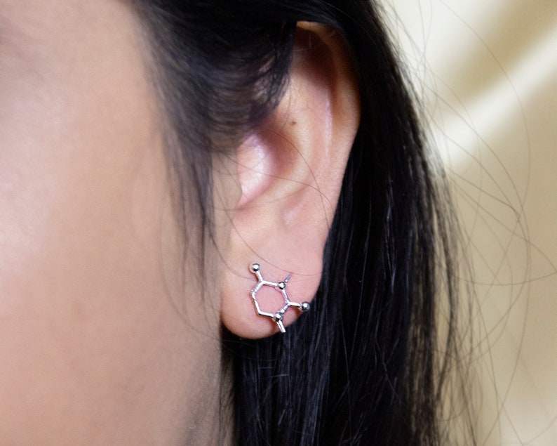 May include: A silver earring shaped like a chemical molecule. The earring is worn in the left ear of a person with long black hair.