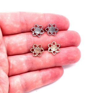 May include: A pair of earrings featuring a silver and gold atom design. The earrings are shown on a hand.