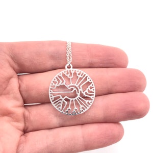 May include: A silver necklace with a circular pendant featuring a detailed tree of life design.