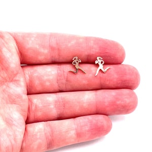 Puede incluir: Un par de pendientes de color dorado con un diseño de silueta de mujer corriendo.