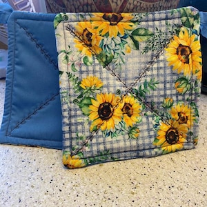 May include: Two blue and white pot holders with a sunflower pattern. The pot holders are quilted and have a checkered pattern.