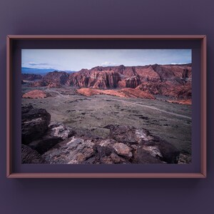 Peut inclure: Une vue panoramique d'un paysage désertique avec des formations rocheuses rouges au loin. Au premier plan, un paysage rocheux et aride avec quelques plantes éparses.