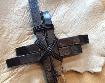 Pode incluir: Uma cruz de metal preto envolvida em arame farpado. A cruz é feita de várias peças de metal empilhadas umas sobre as outras.