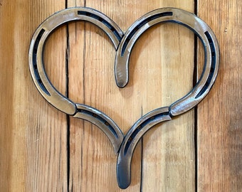 Pode incluir: Decoração de parede em forma de coração feita com ferraduras de metal. As ferraduras prateadas, com detalhes escuros, são montadas sobre um fundo de madeira. Uma decoração rústica e charmosa.