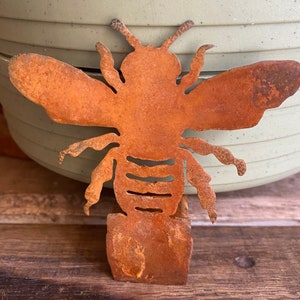 May include: Rusty metal bee garden stake with a cutout design. The bee is standing on a base with a rustic finish.