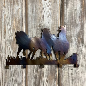 May include: Metal wall hook with a silhouette of three horses running. The hook is brown with a blue and purple iridescent finish. It has four hooks on the bottom.
