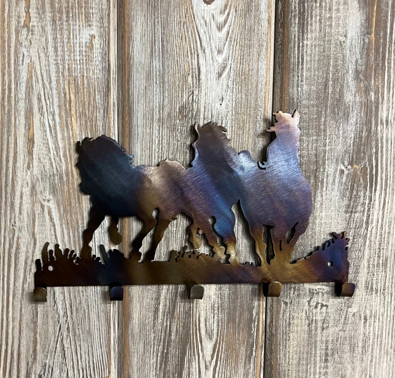 May include: Metal wall hook with a silhouette of three horses running. The hook is brown with a blue and purple iridescent finish. It has four hooks on the bottom.