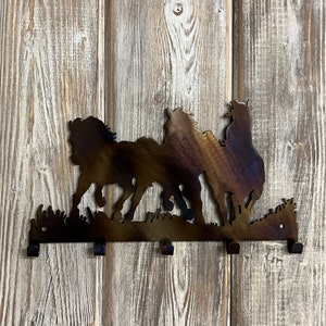 May include: Metal wall mounted key holder with a silhouette of three horses running. The key holder has five hooks.